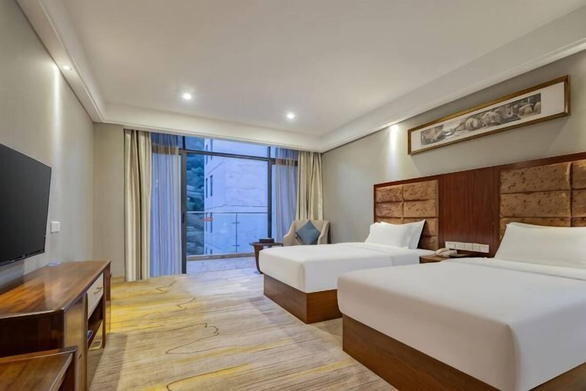 Habitación de hotel con dos camas, televisión, escritorio y un ventanal con cortinas.