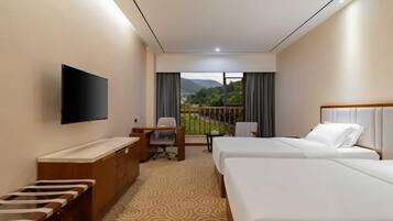 Quarto de hotel com duas camas, uma escrivaninha, televisão e vista para áreas verdes e montanhas.