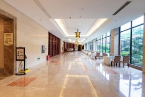 A hotel corridor with a long reception desk, seating area, and large windows offering a view of greenery. - Wufeng International Hotel (Wufeng)