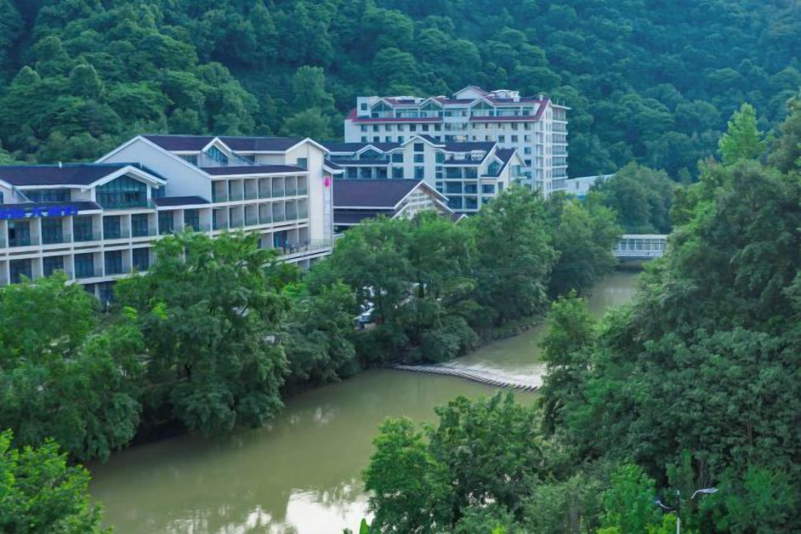 Ein Hotel am Flussufer mit mehreren Gebäuden, einer Brücke und dichter Bepflanzung.