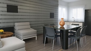 Une cuisine moderne avec un coin repas, comprenant un mur à motifs gris, un canapé gris, une table en verre avec des chaises et un réfrigérateur noir.