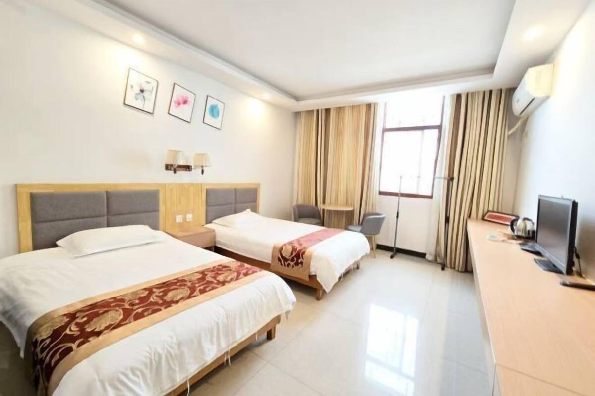 Habitación de hotel con dos camas, un escritorio, un televisor y una ventana con cortinas.
