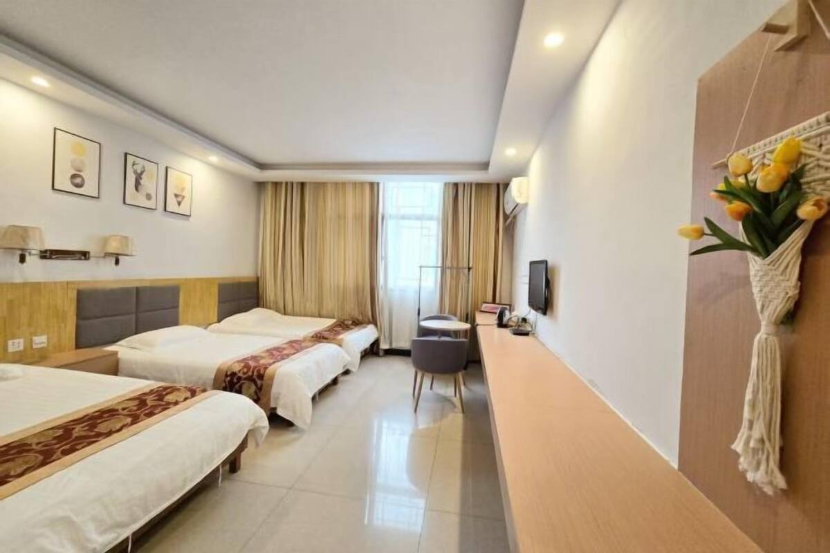 Habitación de hotel con dos camas, un escritorio, una silla, un televisor y un colgador decorativo de macramé.