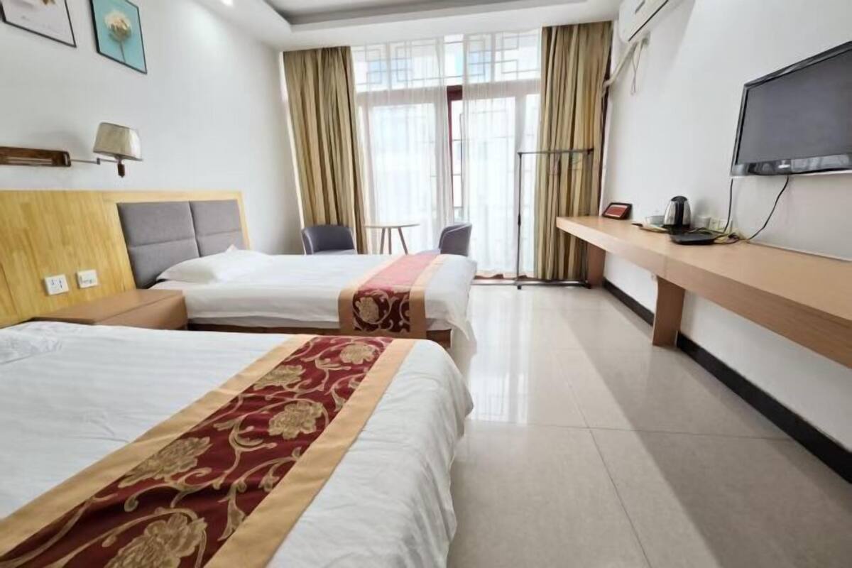 Habitación de hotel con dos camas, un escritorio, una silla, un televisor y una ventana con cortinas.