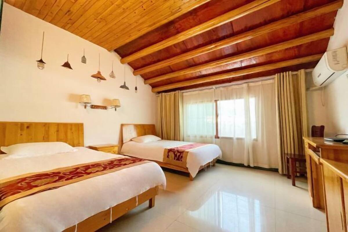 Habitación de hotel con dos camas, vigas de madera en el techo, un escritorio con sillas y una ventana con cortinas.