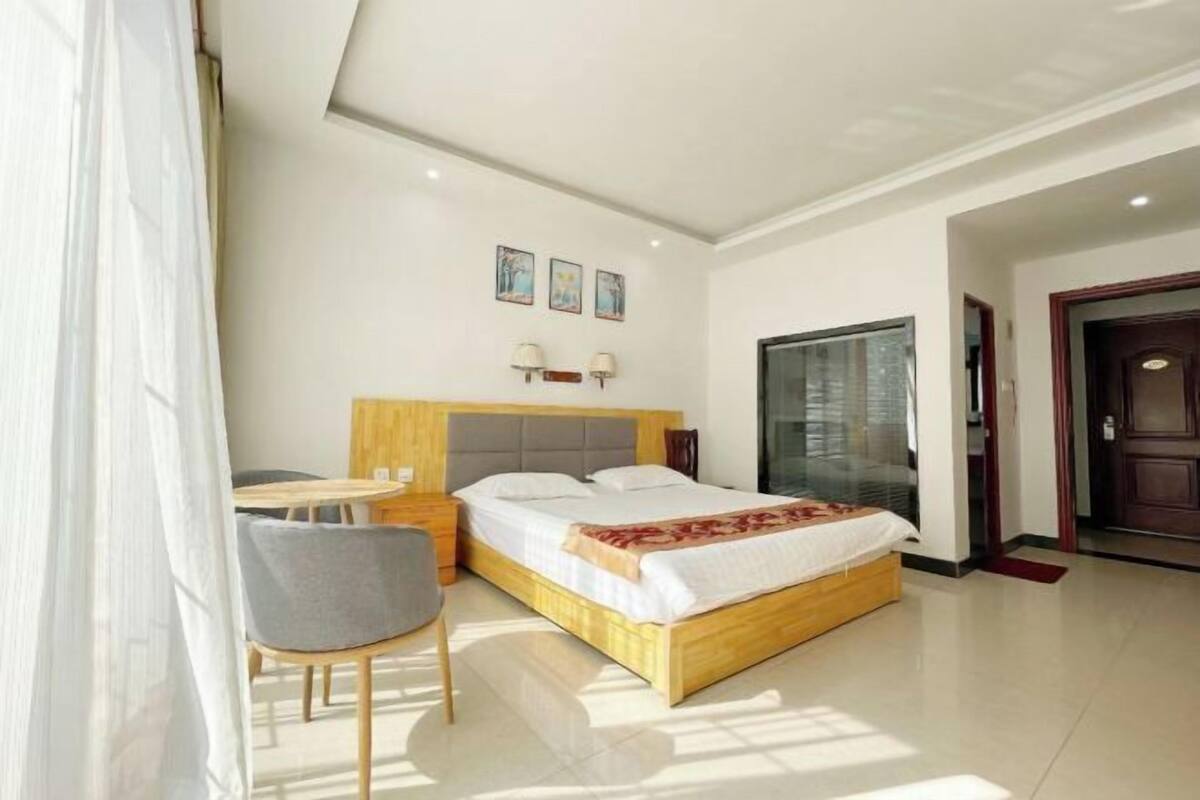 Habitación de hotel con cama, mesita de noche, silla y un amplio ventanal.