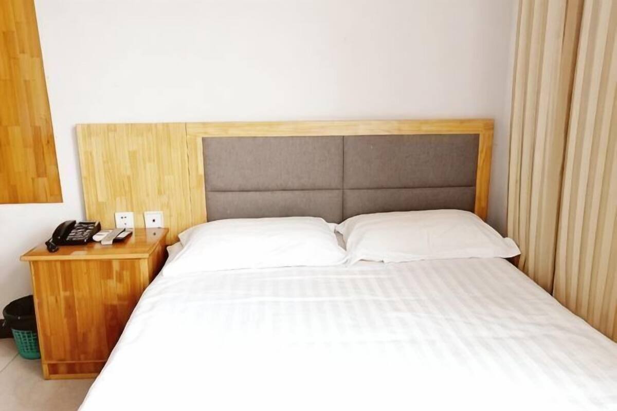 Una habitación de hotel con una mesita de noche de madera, un teléfono y un cubo de basura.