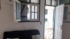 A room with a black sofa, two patterned pillows, a white door, and a window with blinds. - Residence KAYA, Marie-Galante, sea view (Grand-Bourg)