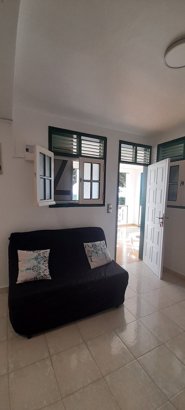 A room with a black sofa, two patterned pillows, a white door, and a window with blinds.