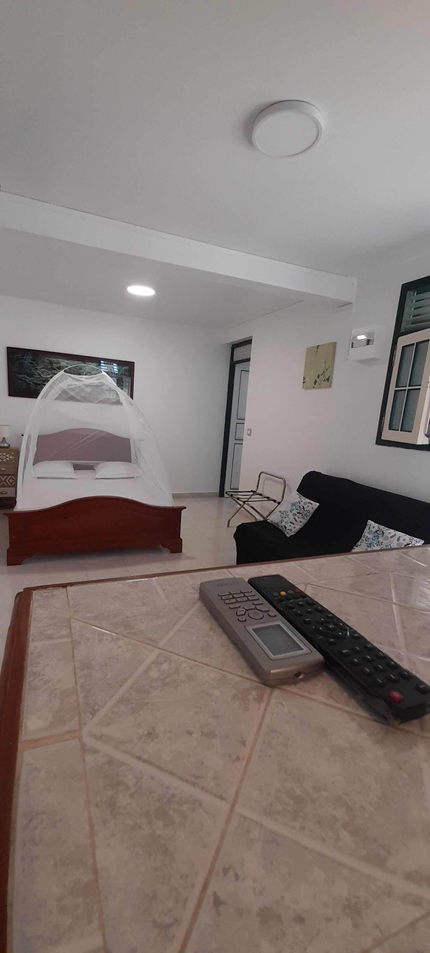 Une chambre à coucher avec un lit, une table de chevet avec une télécommande, une chaise et une porte.