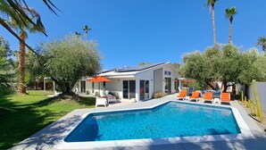 Una casa moderna con piscina, mobiliario exterior y palmeras.