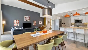 Una sala de estar moderna con una mesa de comedor de madera, sillas verdes, un sofá y un televisor.