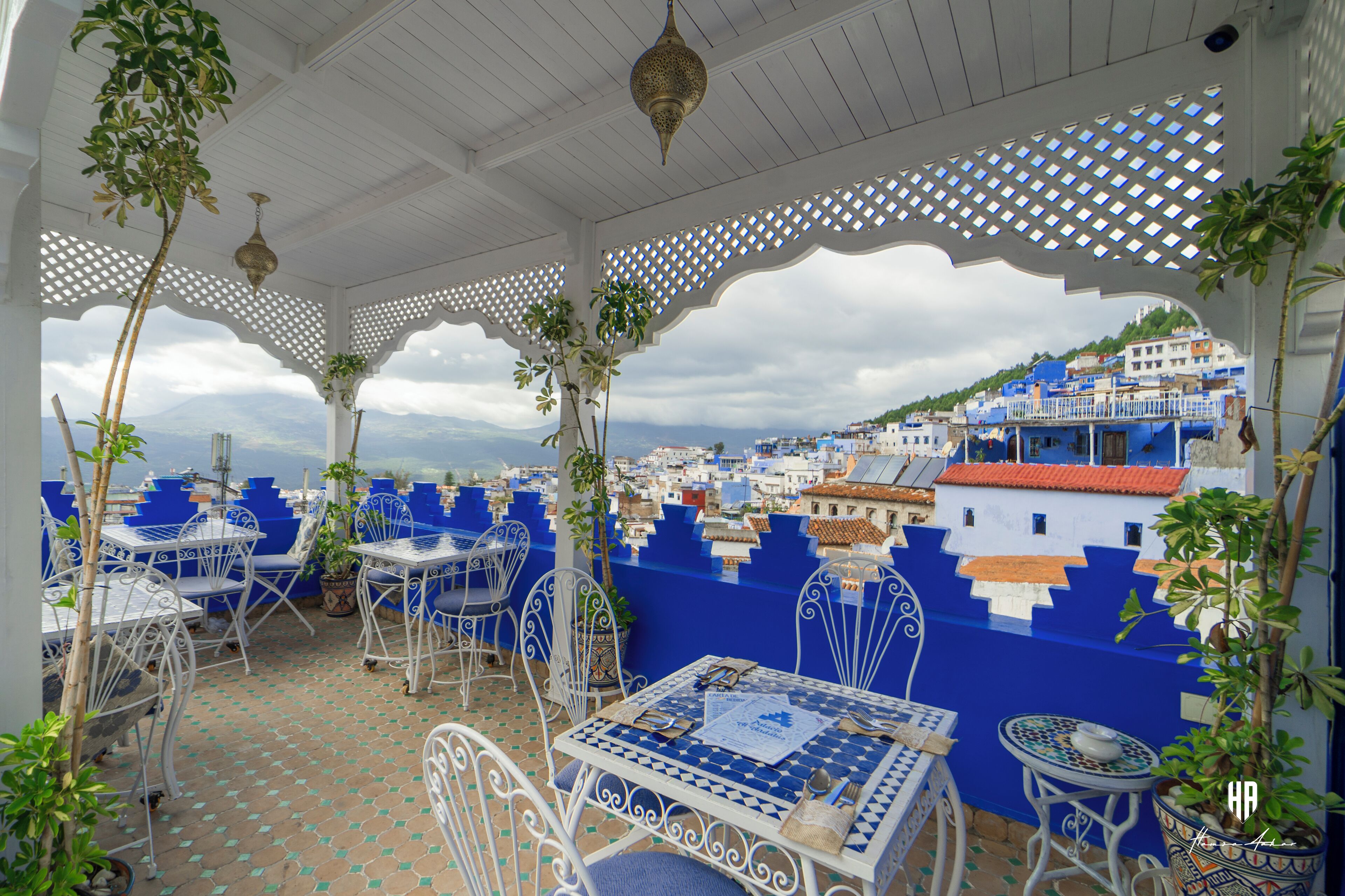 A covered outdoor seating area with tables and chairs, overlooking a cityscape.