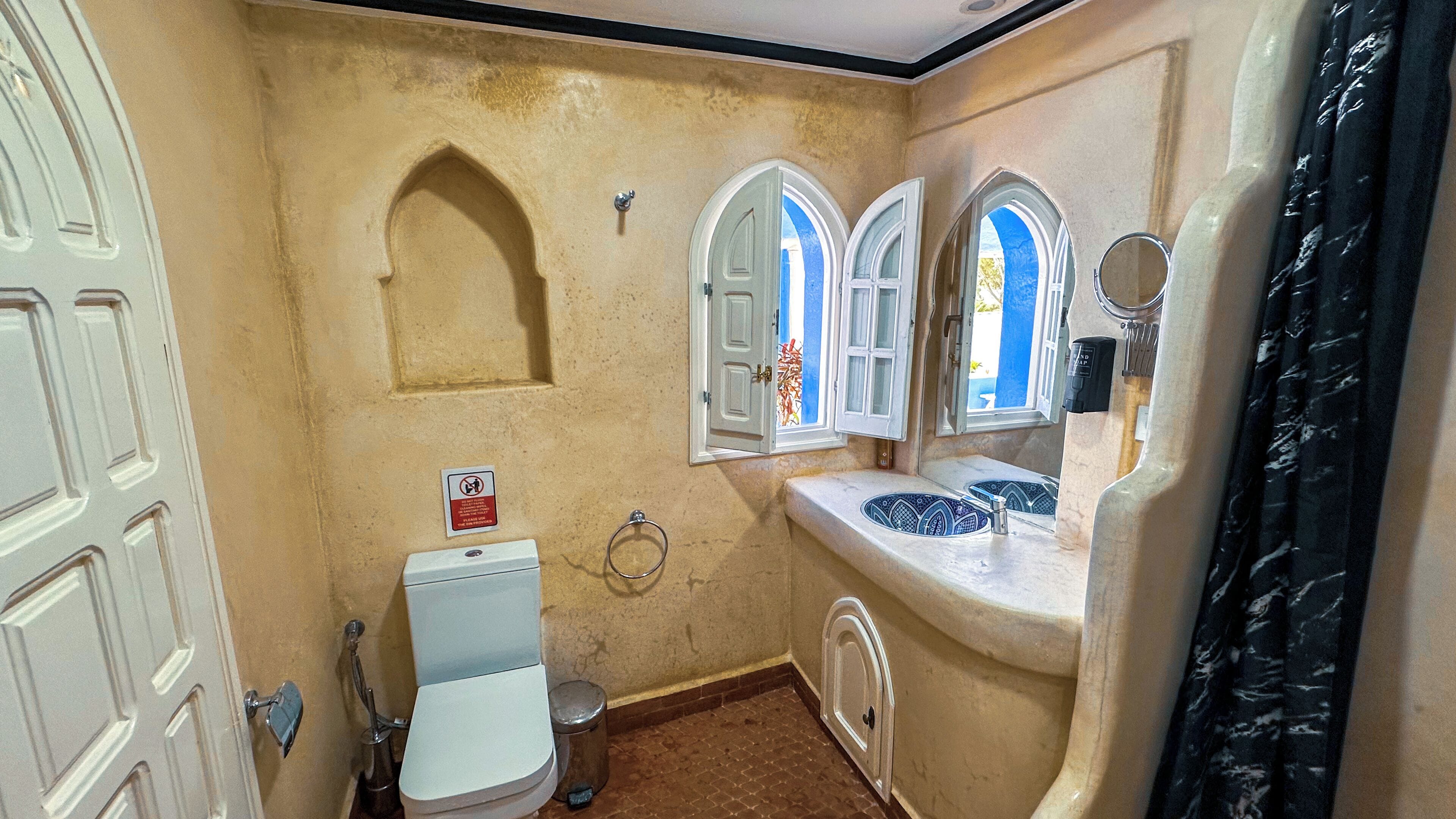 A compact bathroom with a toilet, a sink with decorative tiles, and two arched windows.