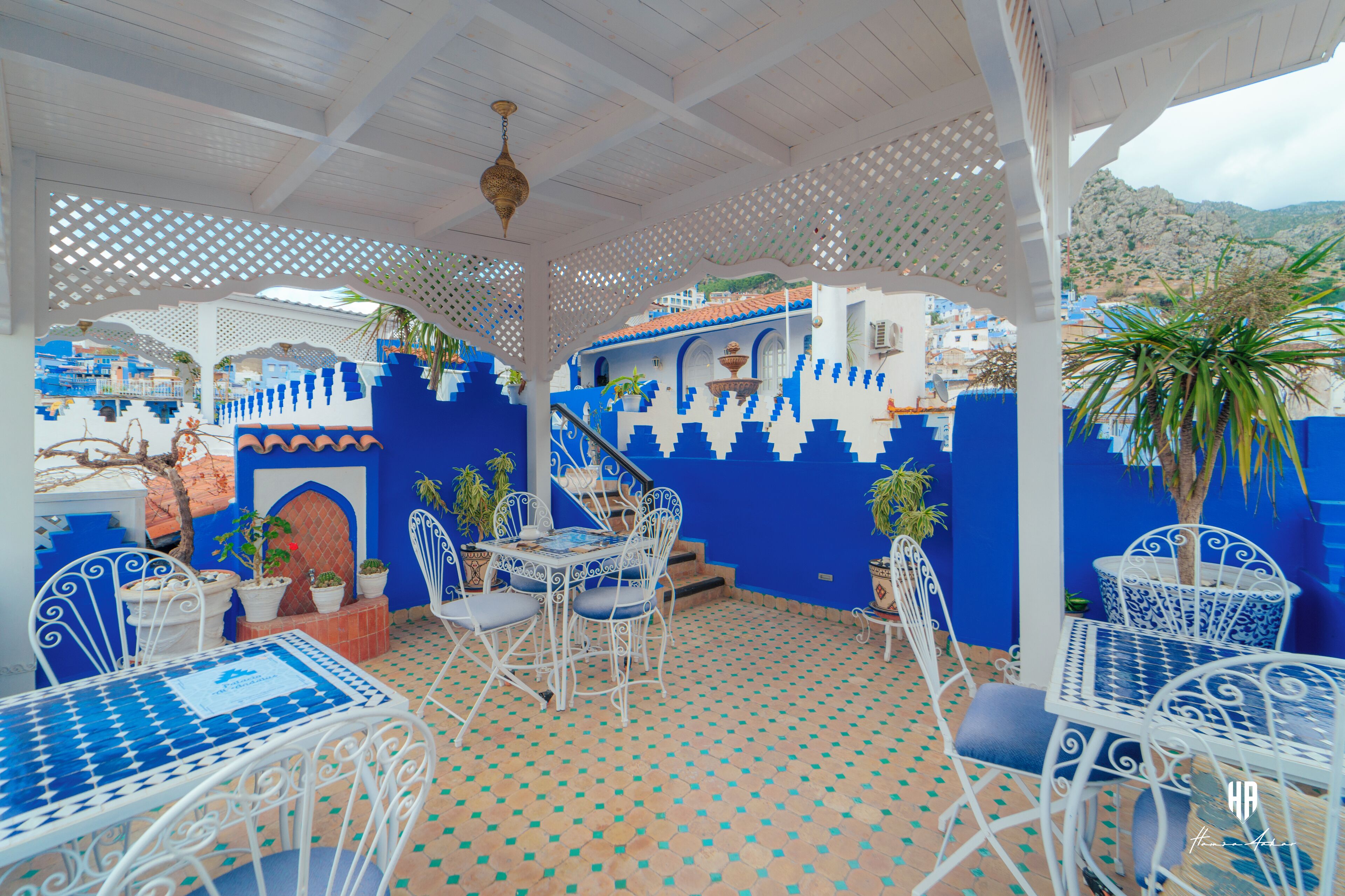 Un patio exterior con mobiliario de metal blanco, paredes azul y blanco, y suelo estampado.