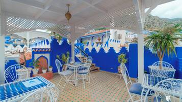 Un patio exterior con mobiliario de metal blanco, paredes azul y blanco, y suelo estampado.