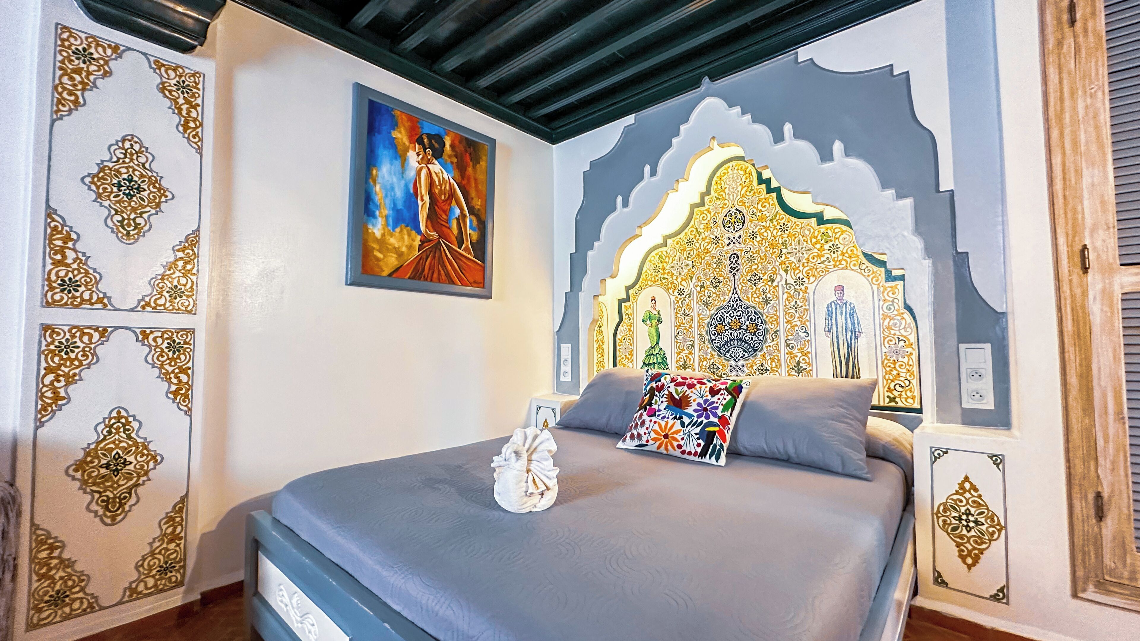 A bedroom with a bed, a painting, and a decorative wall.