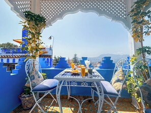 A terrace with a table set for two, blue walls, and a view of the city and mountains. - Palacio Al Andalus (Chefchaouen)