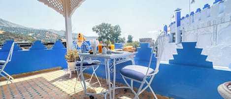 Una terraza con mesa dispuesta para comer, rodeada de paredes pintadas de azul y una pérgola blanca decorativa.
