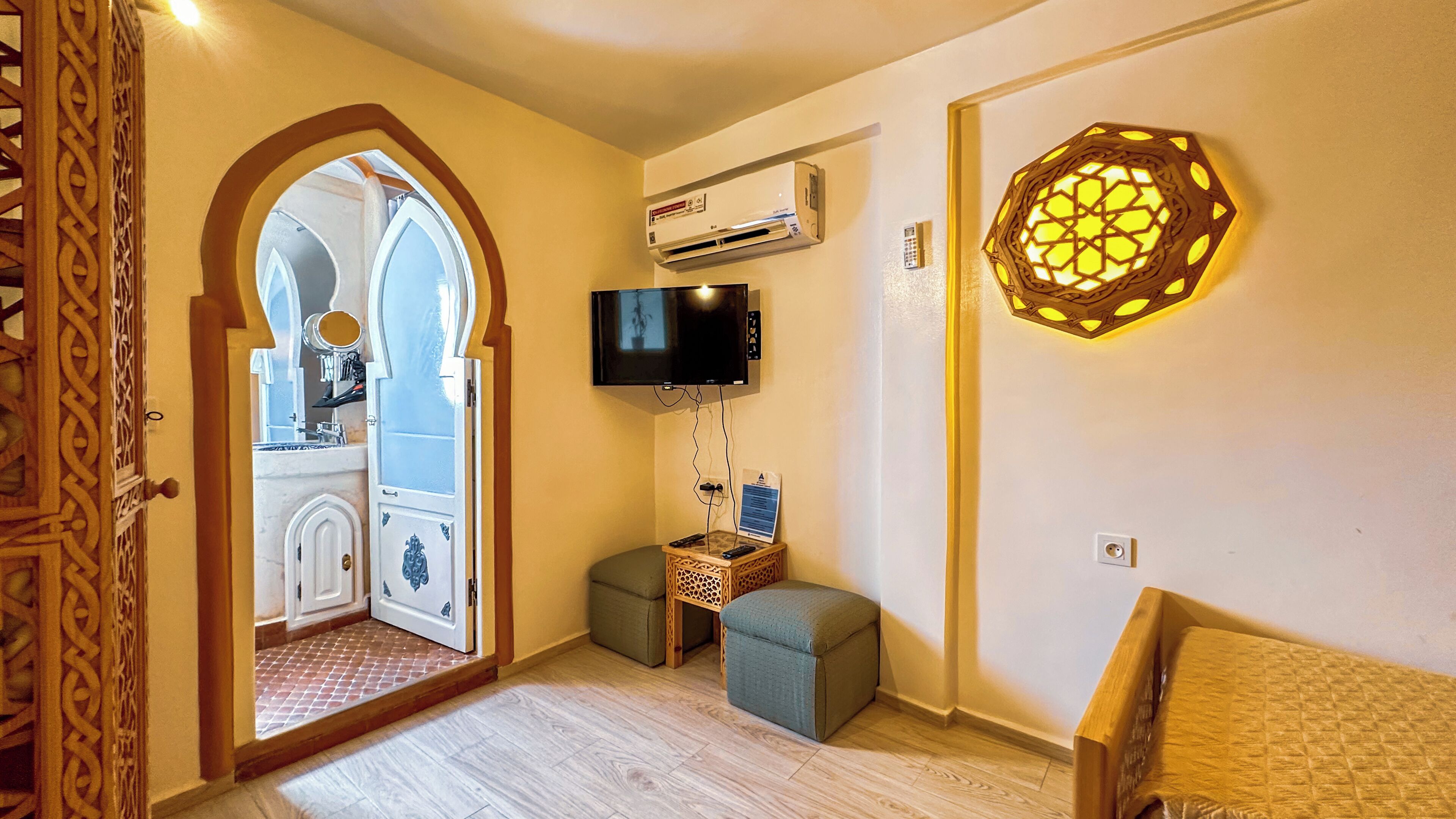 Una habitación con una televisión montada en la pared, una lámpara de pared decorativa y una puerta de madera con elaborados adornos.