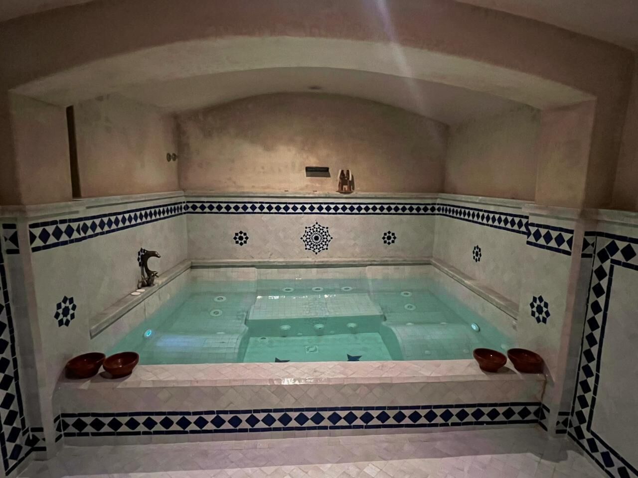 Un bain à remous bordé de carreaux, une petite étagère avec un objet décoratif et deux bols placés sur le bord.