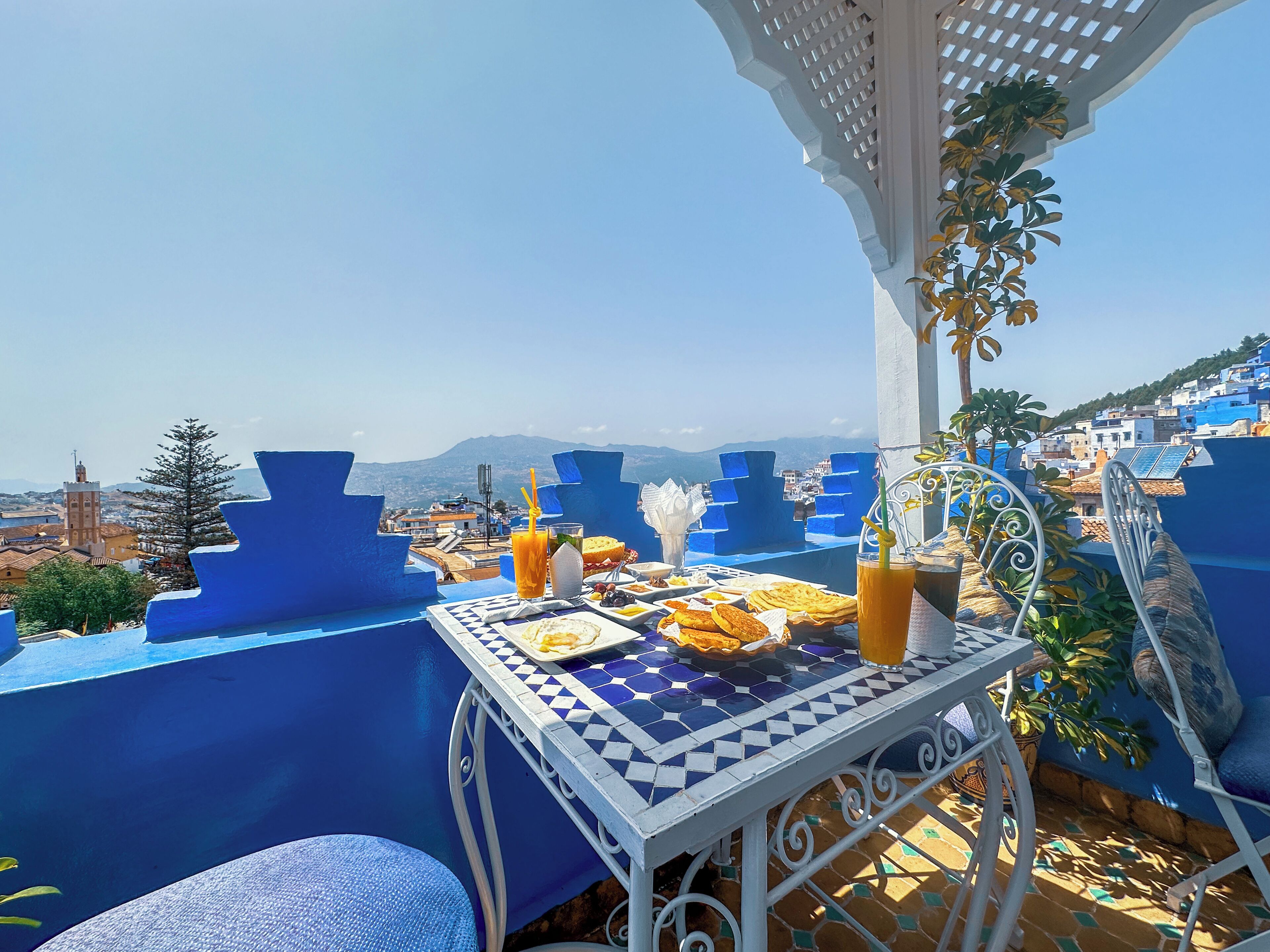 Una mesa con comida y bebidas en una terraza con vistas a un pueblo y montañas.