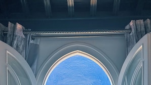 Een kamer met een groot rondboogvenster met uitzicht op een blauw gebouw met een toren.