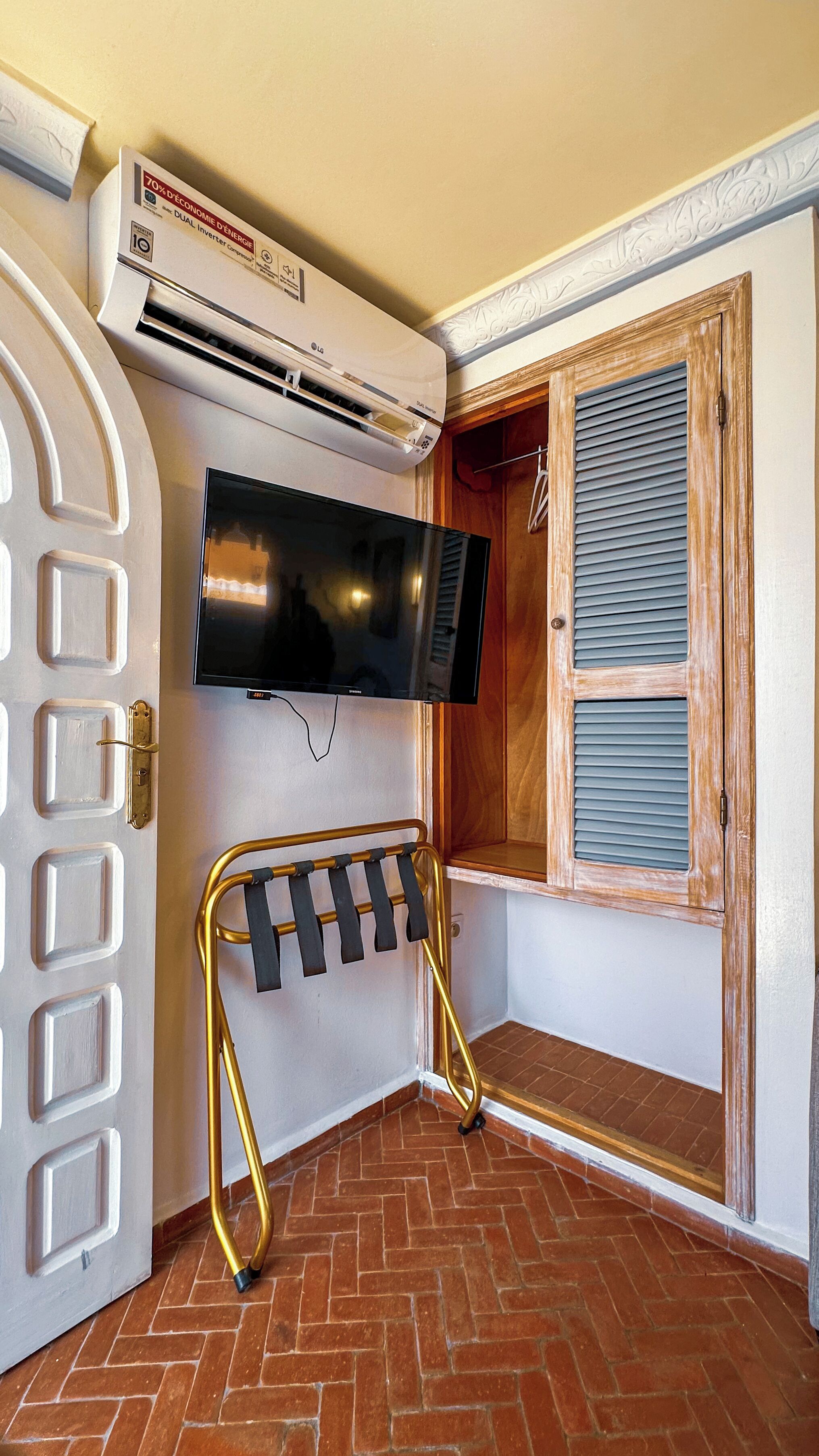 A corner room with a TV mounted on the wall, a built-in wardrobe with a mirror, and a brick floor.