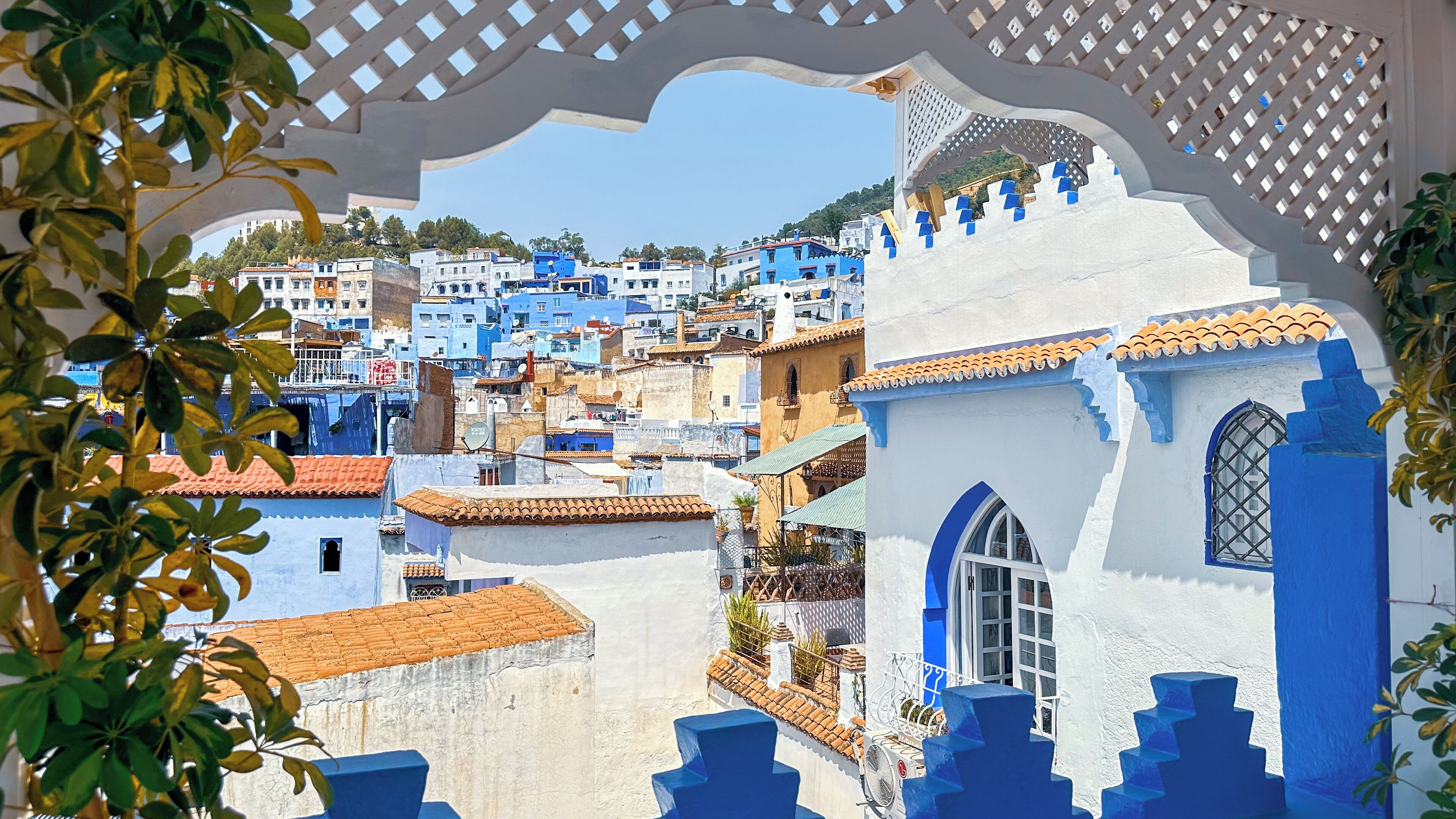 A view of a coastal town with white and blue buildings, a white wall with a window, and a blue staircase.