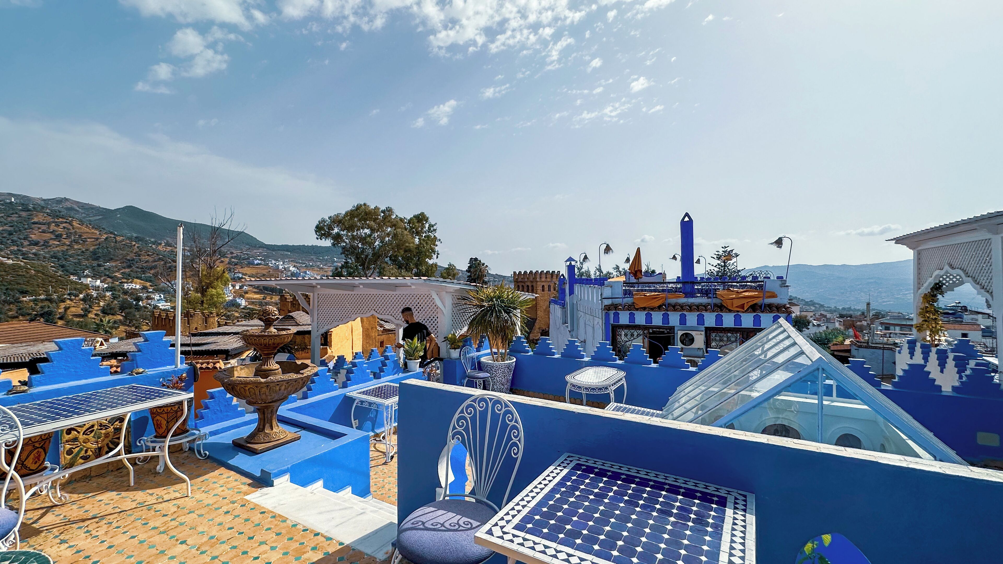 Une terrasse sur le toit, décorée de bleu et de blanc, avec une fontaine et une vue sur la ville et les montagnes.