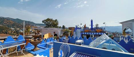 Une terrasse sur le toit, décorée de bleu et de blanc, avec une fontaine et une vue sur la ville et les montagnes.