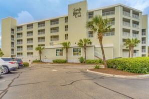 A multi-story hotel with a sign reading "Sands Beach Club." There are several balconies, a parking lot with cars, and palm trees. - On-Site Ocean Access: Condo in Myrtle Beach (Myrtle Beach)