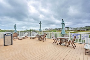 Relax on the deck overlooking the water with lounge chairs and tables, shaded by umbrellas.