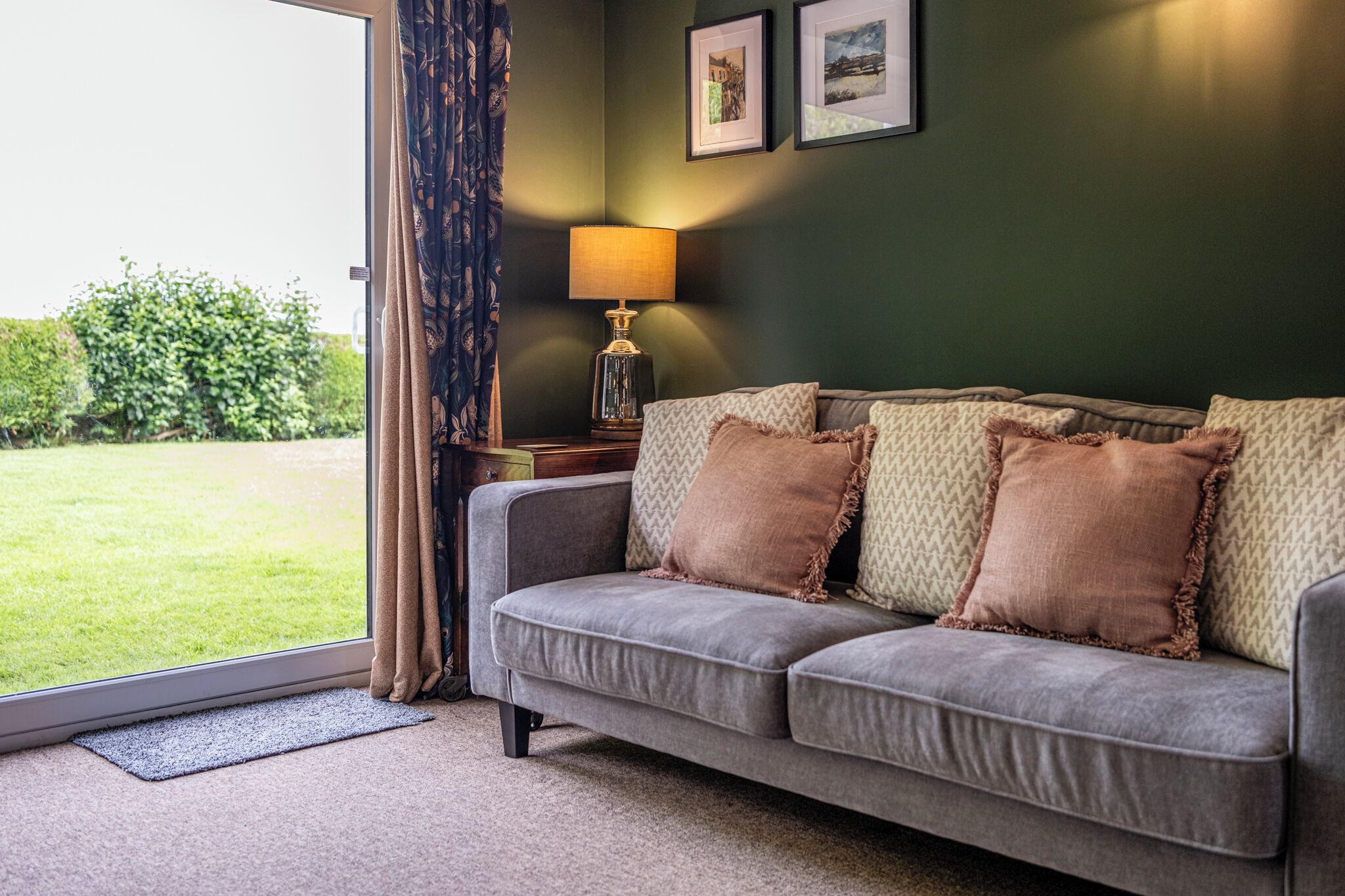 A grey sofa with patterned cushions, a lamp on a side table, and framed pictures on the wall.