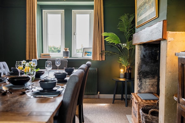 A dining area with a wooden table set for a meal, a fireplace, and a view of the outdoors through a window. - Gorgeous Rural 4BD Farm With Hot Tub (Bath)