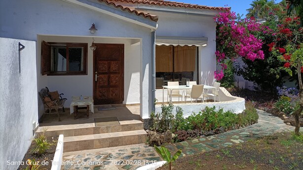 A white building with a tiled roof, a wooden door, and a covered patio with outdoor furniture. - Beautiful apartment with garden and jacuzzi in Puerto de la Cruz (Puerto de la Cruz)