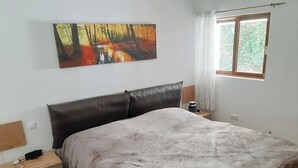 A bedroom with a bed, a nightstand, a bedside table, a wall-mounted painting, and a window with curtains. - Beautiful apartment with garden and jacuzzi in Puerto de la Cruz (Puerto de la Cruz)