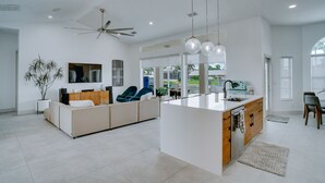 Una cocina moderna con una isla central, un ventilador de techo, luces colgantes y vistas al exterior.