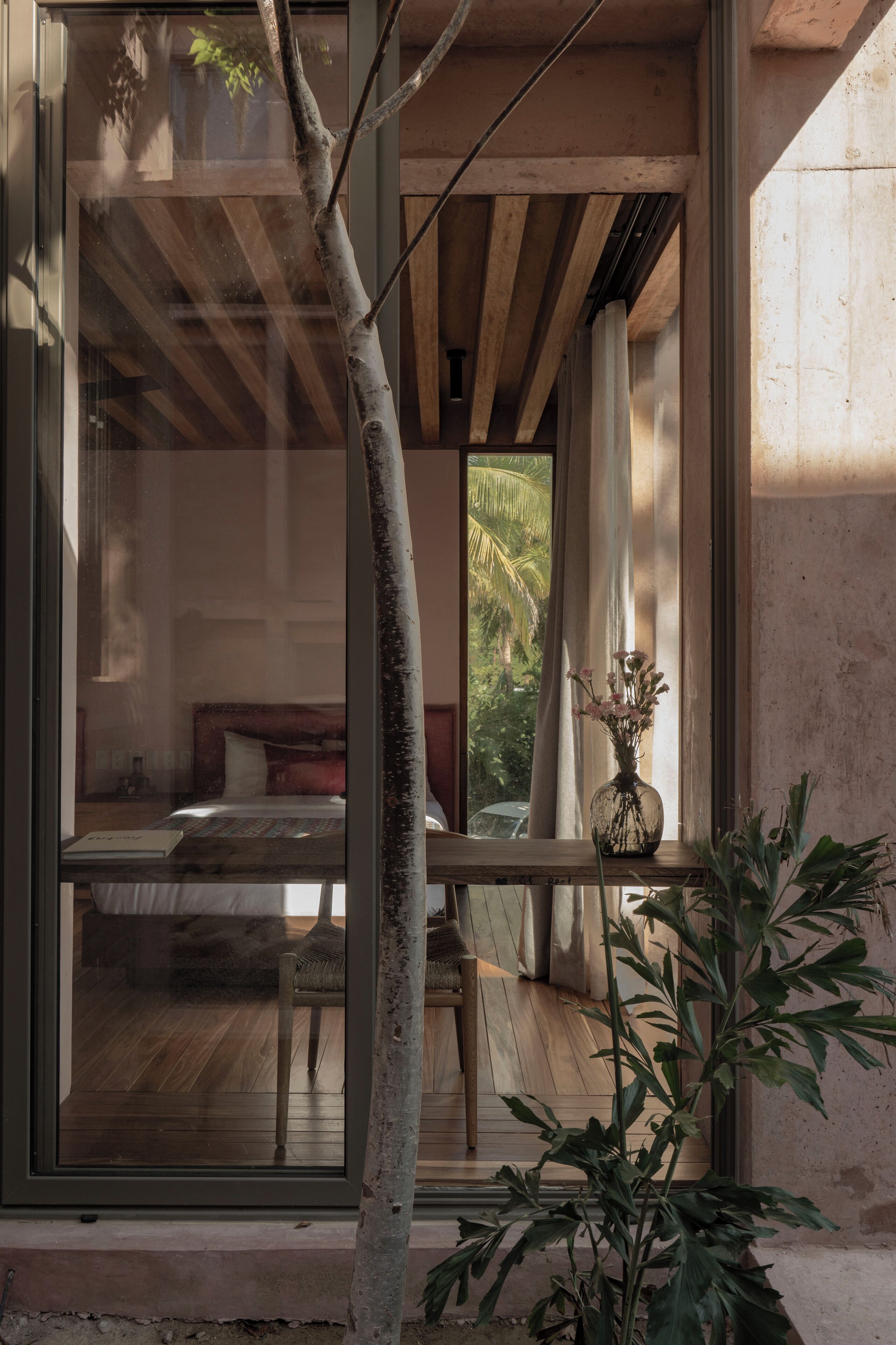 Una habitación con una cama, una mesa con un florero y una ventana con vistas a la vegetación.