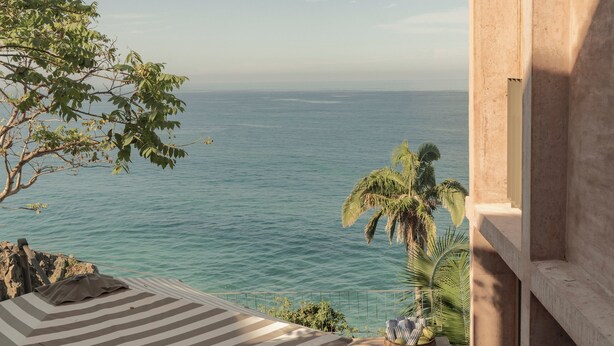 Un espace de restauration en plein air avec vue sur la mer, agrémenté d’un auvent à rayures et d’une table dressée pour le repas.