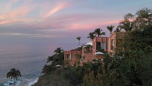 Un bâtiment situé sur la côte, offrant une vue sur l’océan, et entouré de palmiers et de végétation.