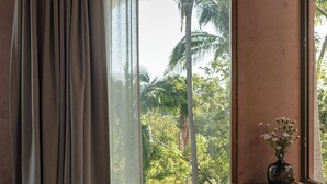Une chambre avec un lit, un bureau, une chaise et une vue sur des palmiers par la fenêtre.