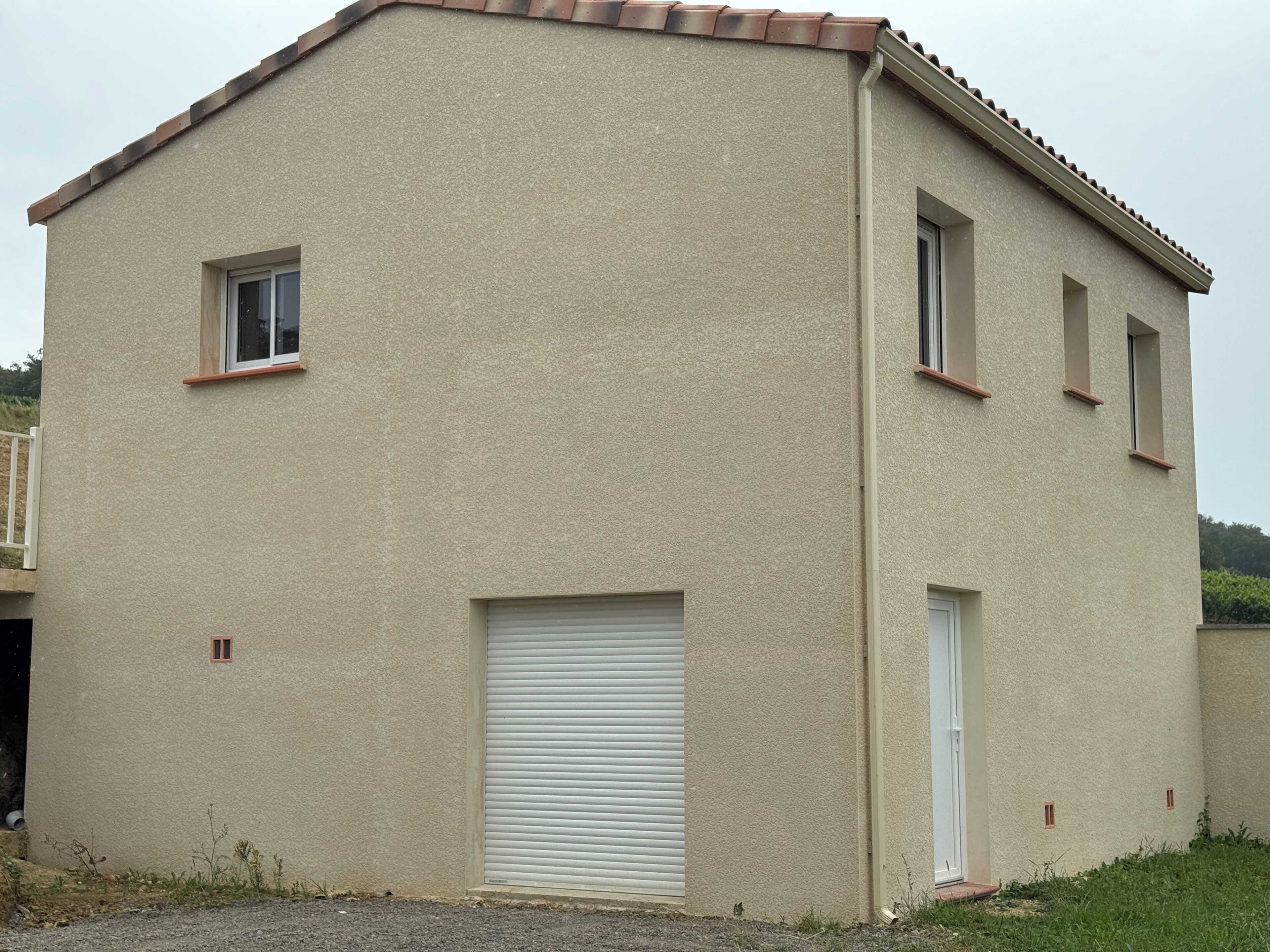 Ein zweistöckiges Gebäude mit beiger Fassade, einer geschlossenen Garagentür und zwei kleinen Fenstern im Obergeschoss.