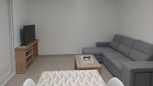 A living room with a grey sofa, a wooden coffee table, a TV on a stand, and a bookshelf. - New house with all comforts! (Ajac)