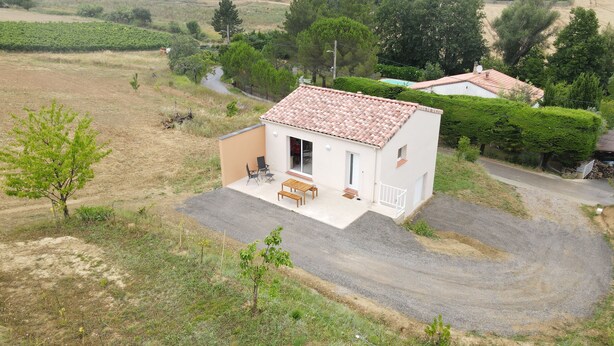 A small house with a tiled roof, a patio with a table and chairs, and a gravel driveway. - New house with all comforts! (Ajac)
