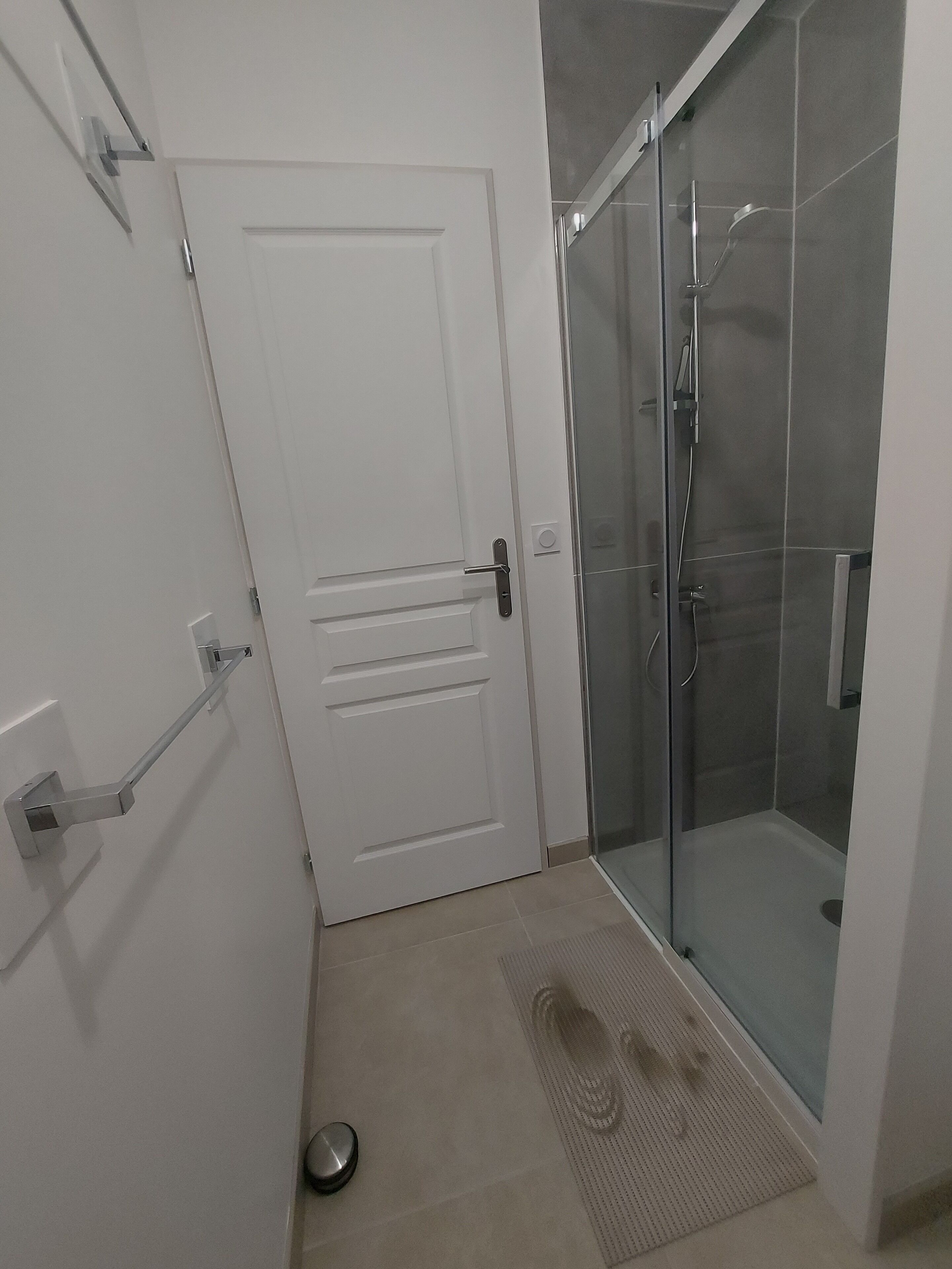 A bathroom with a white door, a glass shower enclosure, and a small mat on the floor.