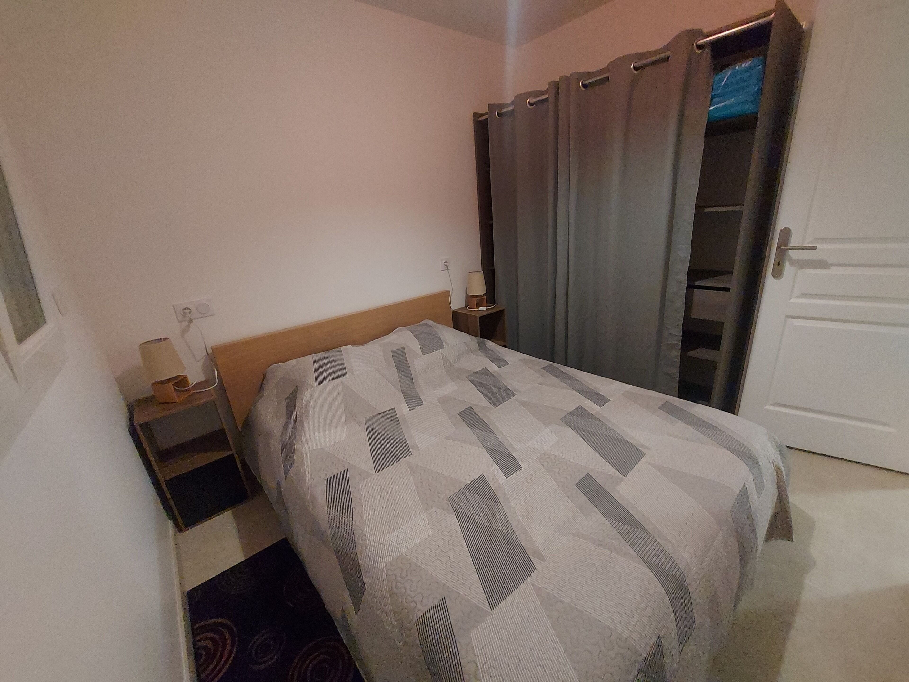 A bedroom with a bed, a nightstand, a lamp, a wardrobe, and a door.
