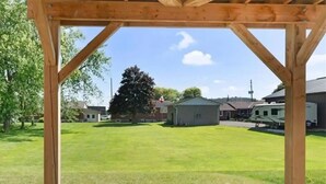 A wooden pergola structure with a clear view of a well-maintained lawn and a small building in the background. - Classy Home Near Beach & Airport

 (Hagersville)