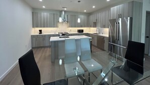 Une cuisine moderne dotée d’un îlot central, d’appareils électroménagers en acier inoxydable et d’une table à manger en verre.