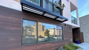 Un bâtiment moderne doté de grandes fenêtres qui reflètent les immeubles voisins et les voitures garées.